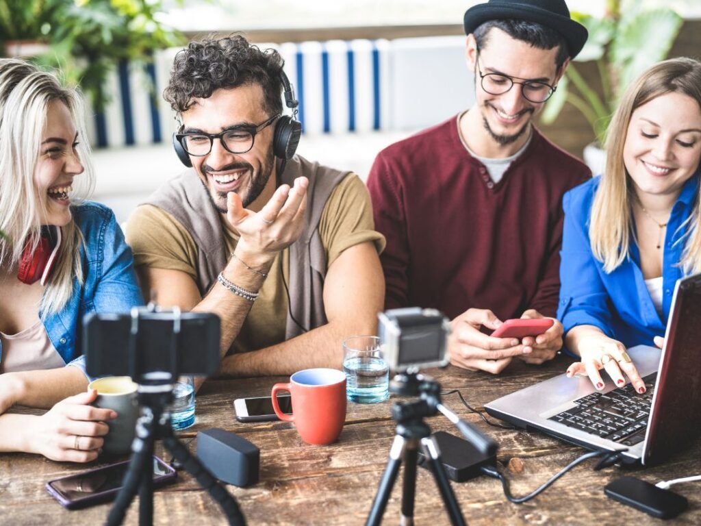 Four people at a table, each with a laptop and camera, engaged in a collaborative discussion or project.