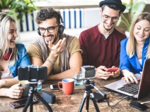 Four people at a table, each with a laptop and camera, engaged in a collaborative discussion or project.