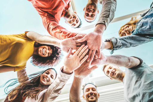 A diverse group of people standing in a circle, joining hands together in a gesture of unity and collaboration.