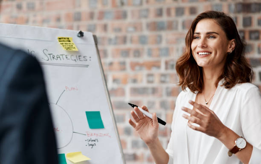 A woman discusses ideas with a man in front of a whiteboard filled with notes and diagrams.